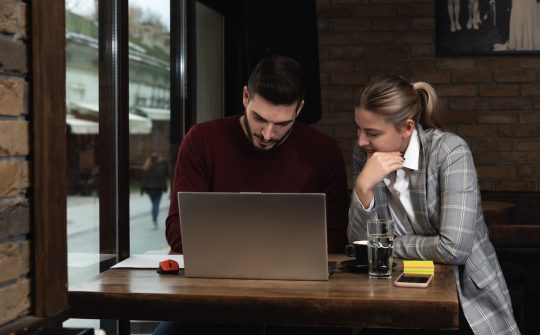 Two young business partners man and woman sitting in cafeteria working on the new project while they drinking coffee and exchanging ideas and plans for better performance of their company.